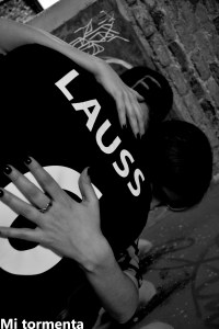 Mi Tormenta, la imagen en blanco y negro, muestra un abrazo. Solo podemos ver la espalda de uno de los personajes con una camiseta deportiva con el nombre LAUSS escrito con letras blanca